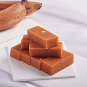 Stack of rectangular Red Banana Mysorepak on a white plate with bananas in the background